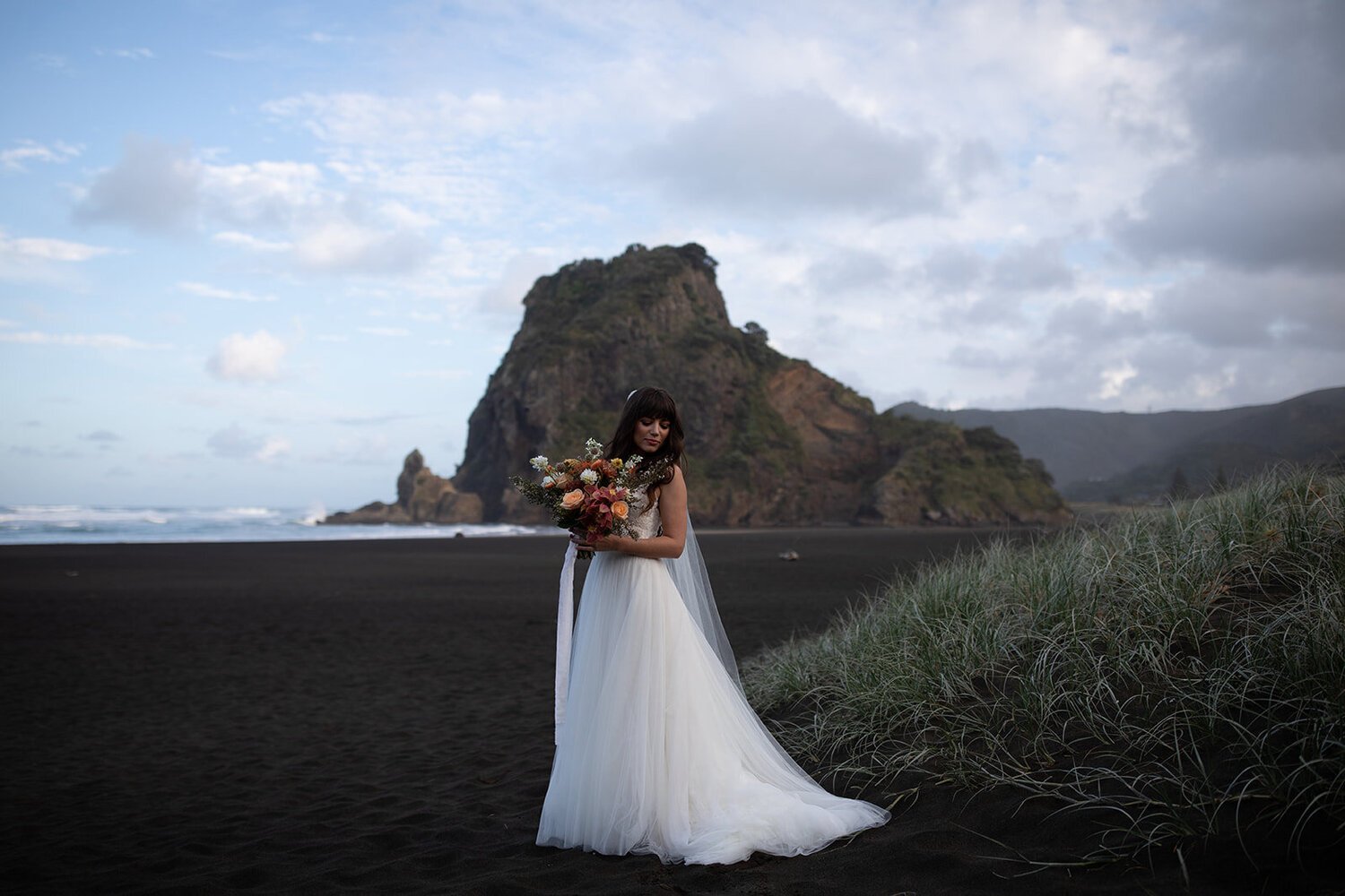 Anni Graham's published before image: a bride on a dark beach beneath a cloudy blue sky.