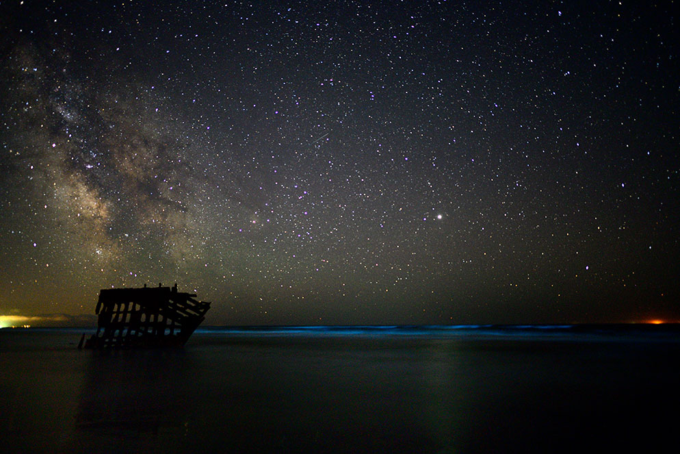 Paul Van Allen night-sky photograph with the Milky Way above a dark shipwreck silhouette and ocean horizon.