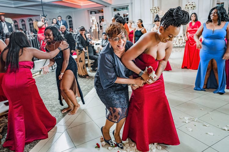 Wedding guests laughing and reaching around a bouquet while other guests watch