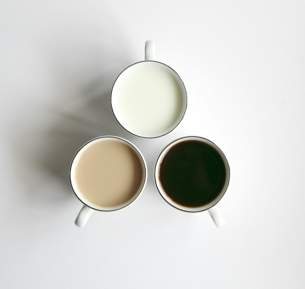 Three white cups with pale, tan and dark drinks arranged in a triangle