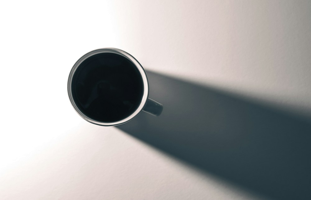 Dark cup casting a long diagonal shadow across a pale surface