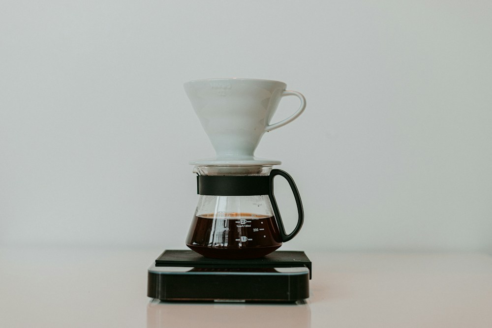 White coffee brewer above a glass server on a black scale, photographed by Szymon Satora.