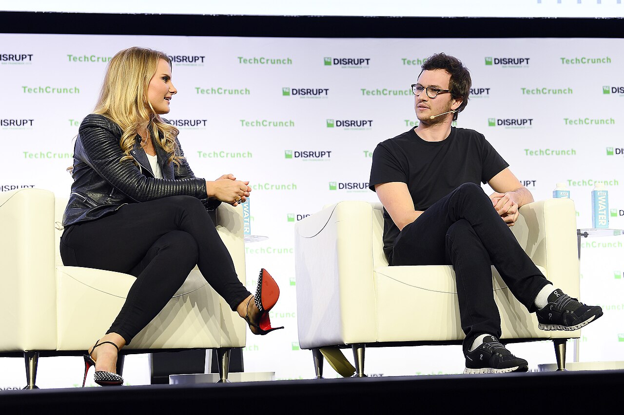 Michele Romanow and Henrique Dubugras seated in conversation on the TechCrunch Disrupt stage, with the event backdrop visible.