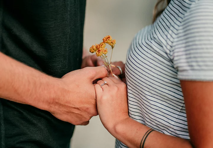 Close view of two people holding hands, showing a ring and small yellow flowers against their clothing.