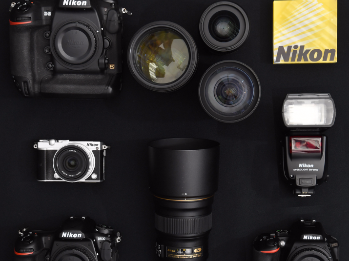 Nikon flat lay of camera bodies, lenses, a flash and a yellow Nikon box on a dark surface
