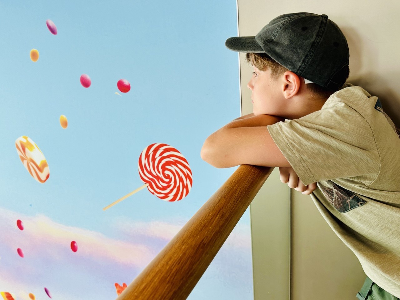 Boy in a baseball cap leaning over a railing while looking at a bright candy-themed wall display